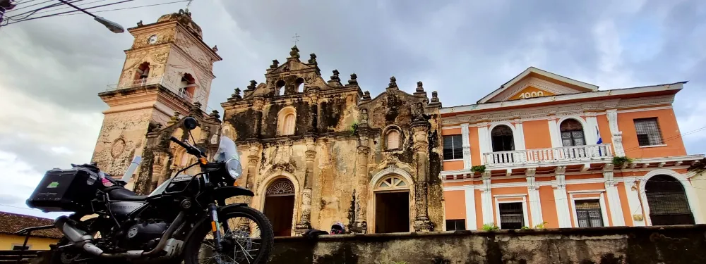 Une moto garée près d'une église coloniale et d'un bâtiment orangé au Nicaragua