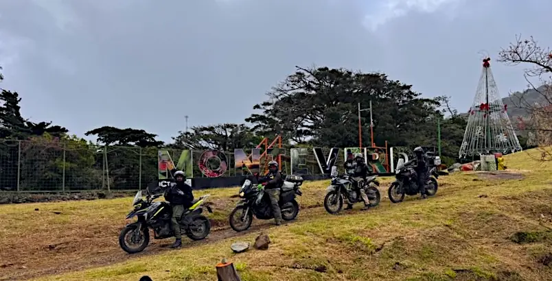 Des motards sur leurs motos devant les grandes lettres de Monteverde