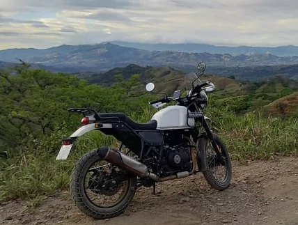 Royal Enfield Himalayan garée sur une piste dominant des vallées verdoyantes et des montagnes