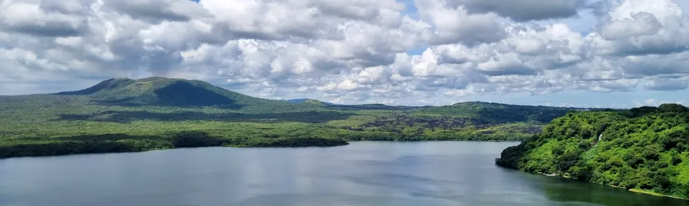 Une étendue d'eau bordée de collines verdoyantes, sous un ciel nuageux