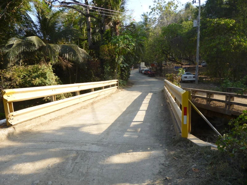 Petit pont sur une route de terre près de l'entrée du sentier, voitures garées plus loin