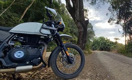 Gros plan sur le moteur, le réservoir et la roue avant de la Royal Enfield Himalayan au bord d'une piste