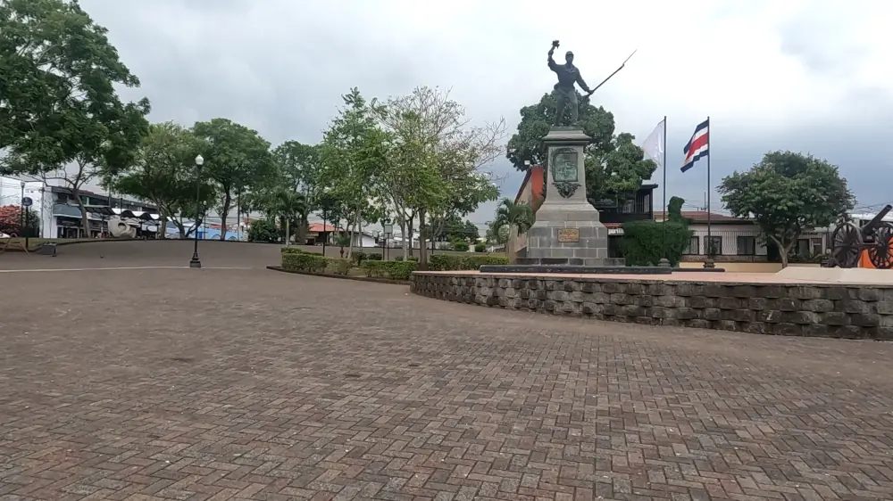 Statue de Juan Santamaría sur une place pavée, à côté du drapeau du Costa Rica et d'un canon