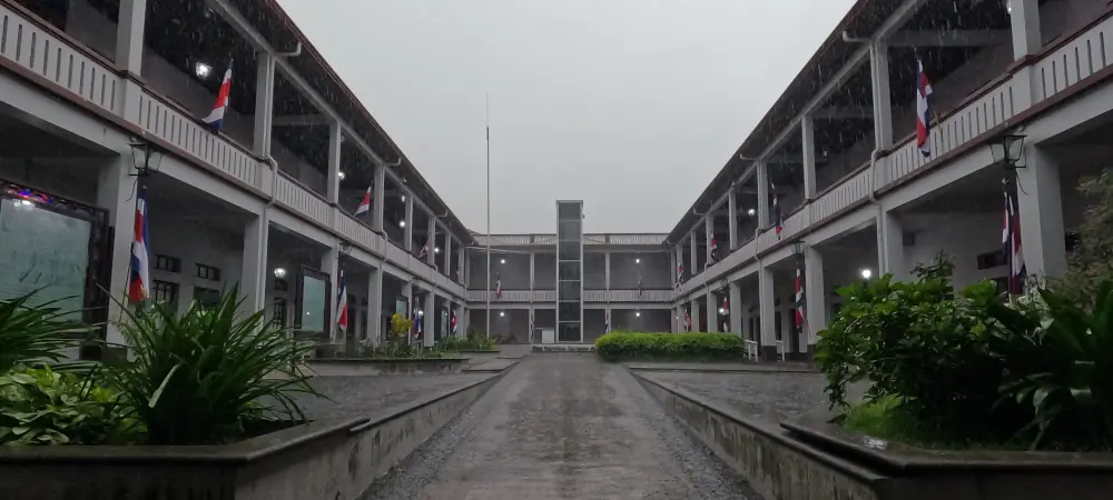 Cour intérieure du musée Juan Santamaría, bordée de galeries pavoisées aux couleurs du Costa Rica, sous la pluie