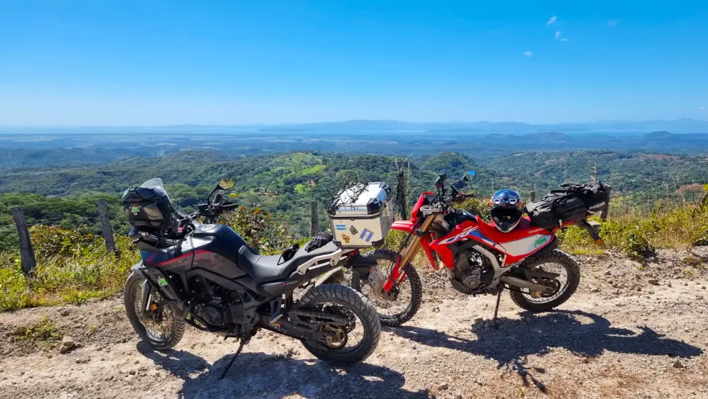 Deux motos trail garées sur une piste, avec vue sur les collines et la côte au loin