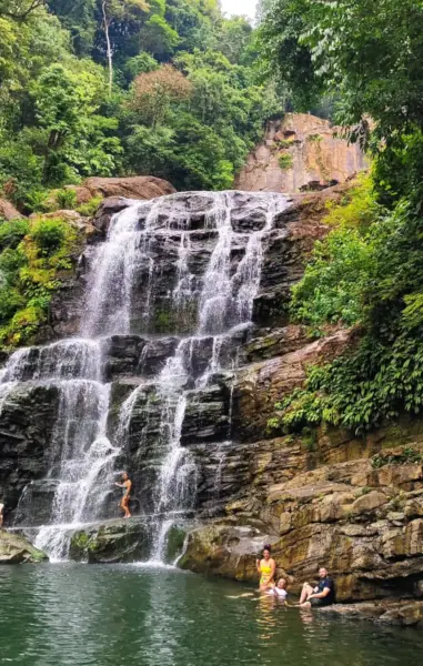 Chute d'eau sur des rochers en gradins entourés de forêt, avec des baigneurs dans la vasque naturelle
